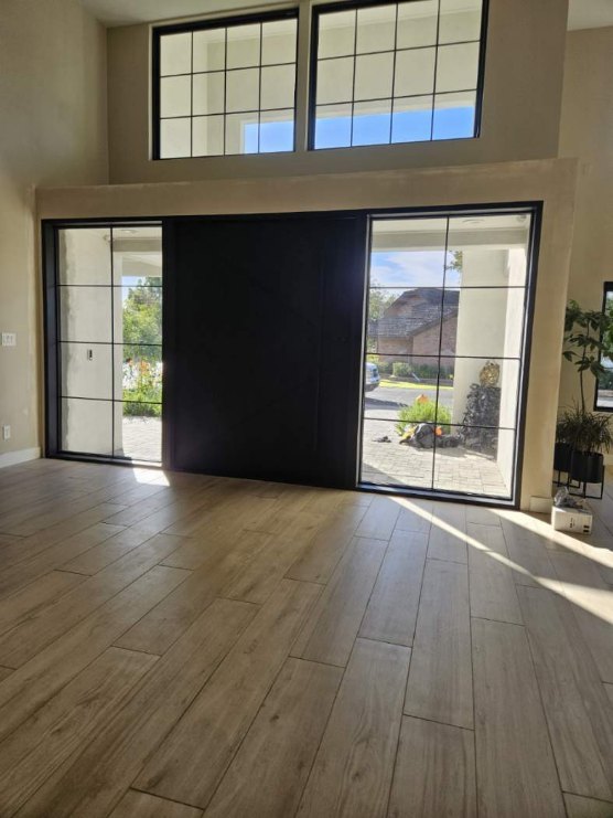 Interior view of a wide black front door centered between tall grid-pane windows, with matching transom windows above.
