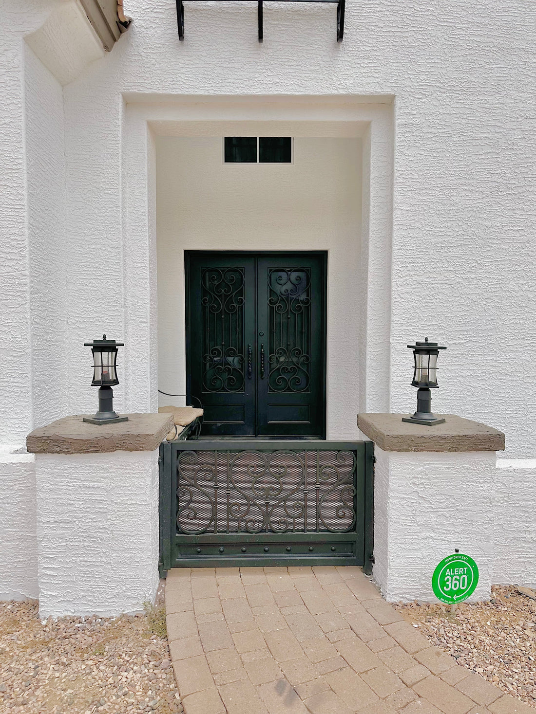 Black wrought iron double doors and a decorative entry gate contrast with a white stucco exterior and stone walkway.