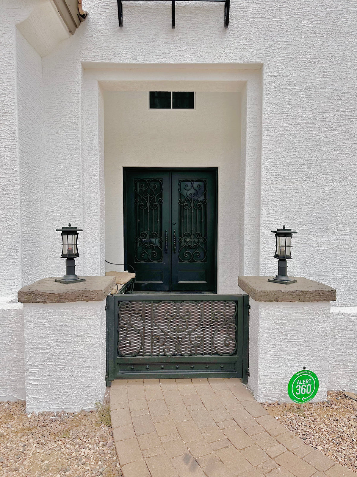 Black wrought iron double doors and a decorative entry gate contrast with a white stucco exterior and stone walkway.
