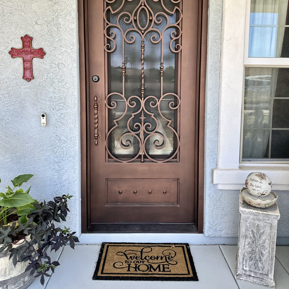 Decorative bronze security door with scroll grille and glass panel above a mat reading “Welcome to our HOME.”