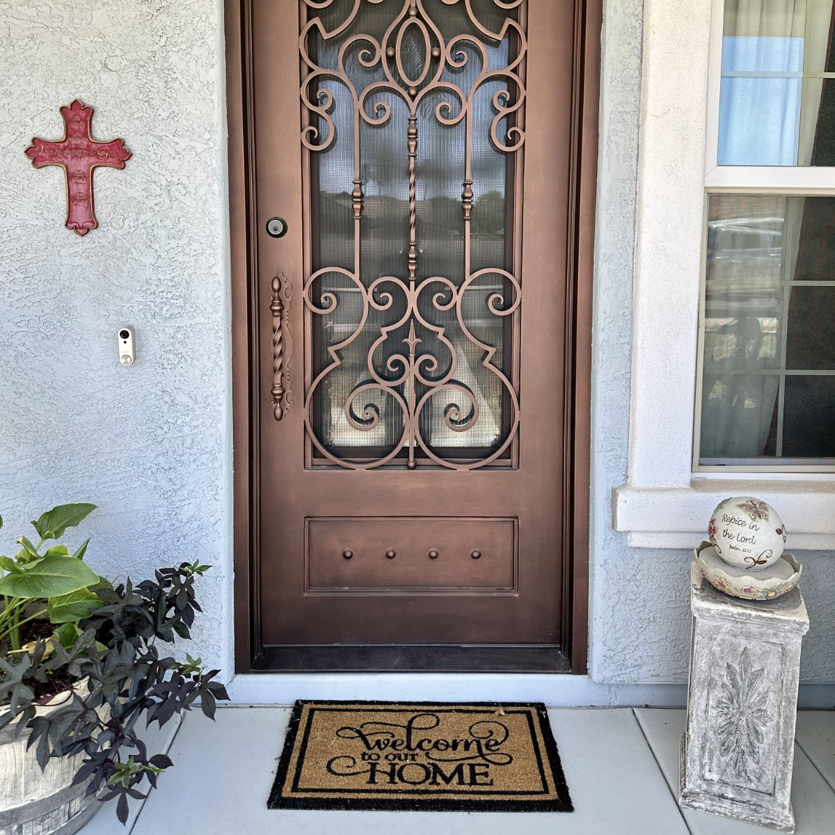 Decorative bronze security door with scroll grille and glass panel above a mat reading “Welcome to our HOME.”